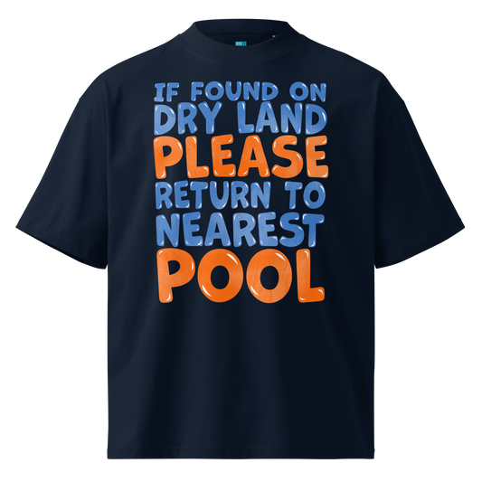 A navy blue short-sleeve organic oversized t-shirt with a bold graphic text print on the front reading 'IF FOUND ON DRY LAND PLEASE RETURN TO NEAREST POOL' in light blue and orange lettering, shown against a plain white background.