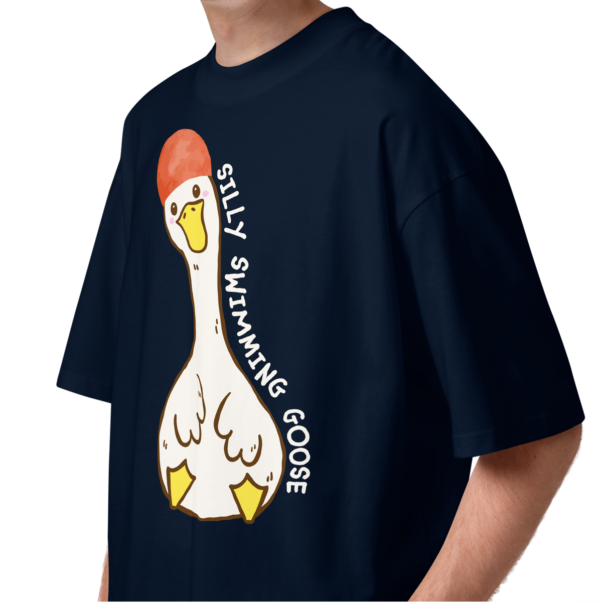 A young man with curly brown hair wearing a navy blue short-sleeve organic oversized t-shirt by Lane Line Threads featuring a cartoon graphic of a white swimming goose wearing a red swim cap, with the text 'SILLY SWIMMING GOOSE' printed vertically alongside it.