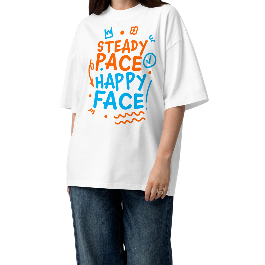 A woman modeling a white short-sleeve crewneck organic oversized t-shirt by Lane Line Threads featuring a colorful graphic print on the front with the words 'STEADY PACE HAPPY FACE' in orange and blue hand-drawn lettering, paired with loose dark blue jeans and brown sandals on a clean white background.