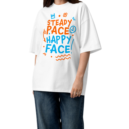 A woman modeling a white short-sleeve crewneck organic oversized t-shirt by Lane Line Threads featuring a colorful graphic print on the front with the words 'STEADY PACE HAPPY FACE' in orange and blue hand-drawn lettering, paired with loose dark blue jeans and brown sandals on a clean white background.