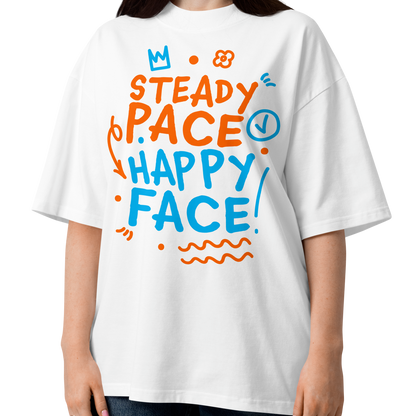 A woman modeling a white short-sleeve crewneck organic oversized t-shirt by Lane Line Threads featuring a colorful graphic print on the front with the words 'STEADY PACE HAPPY FACE' in orange and blue hand-drawn lettering.