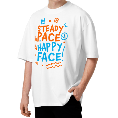 A young man with curly brown hair wearing a white short-sleeve crewneck organic oversized t-shirt by Lane Line Threads featuring a colorful graphic print on the front with the words 'STEADY PACE HAPPY FACE' in orange and blue hand-drawn lettering.