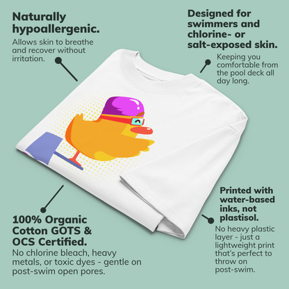 A white organic oversized t-shirt laid diagonally on a pale green background with multiple callout text bubbles describing product benefits. The shirt has a colorful duck graphic printed on the front, with a purple swim cap, yellow-orange duck, and blue/purple pool deck area.