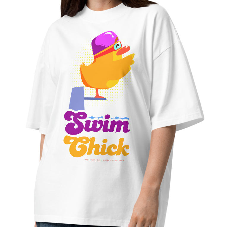 A woman modeling a white short-sleeve crewneck organic oversized t-shirt by Lane Line Threads featuring a colorful graphic of a yellow duck wearing a purple swim cap and goggles, with the text 'Swim Chick' printed below in purple and orange, paired with dark blue jeans and brown sandals, against a plain white background.