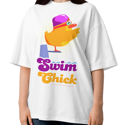 A woman wearing a white short-sleeve crewneck organic oversized t-shirt by Lane Line Threads featuring a colorful graphic of a yellow duck wearing a purple swim cap and goggles, with the text 'Swim Chick' printed below in purple and orange, paired with dark blue jeans against a plain white background.