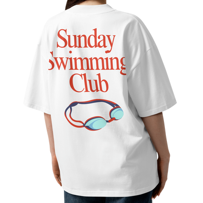 A woman shown from the back wearing a white organic oversized t-shirt with a red graphic text reading 'Sunday Swimming Club' and a blue and red pair of goggles illustration.