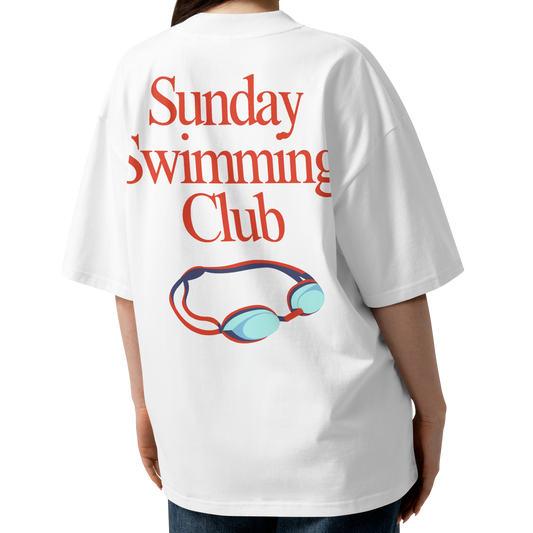 A woman shown from the back wearing a white organic oversized t-shirt with a red graphic text reading 'Sunday Swimming Club' and a blue and red pair of goggles illustration.