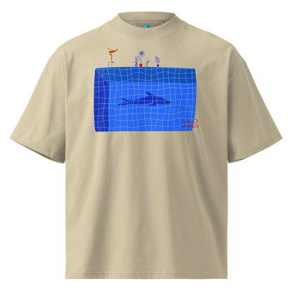 A beige short-sleeve crewneck organic oversized t-shirt by Lane Line Threads for swimmers featuring a graphic print of a blue swimming pool with a diving board, a diver, plants, and a shark on the front.