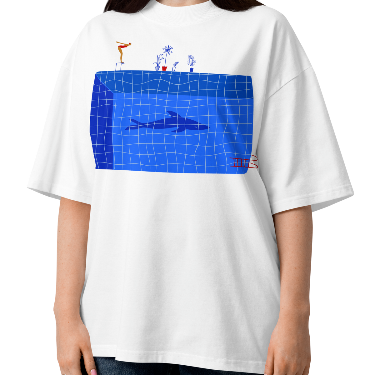 A woman modeling a white short-sleeve crewneck organic oversized t-shirt by Lane Line Threads for swimmers featuring a graphic print of a blue swimming pool with a diving board, a diver, plants, and a shark on the front.