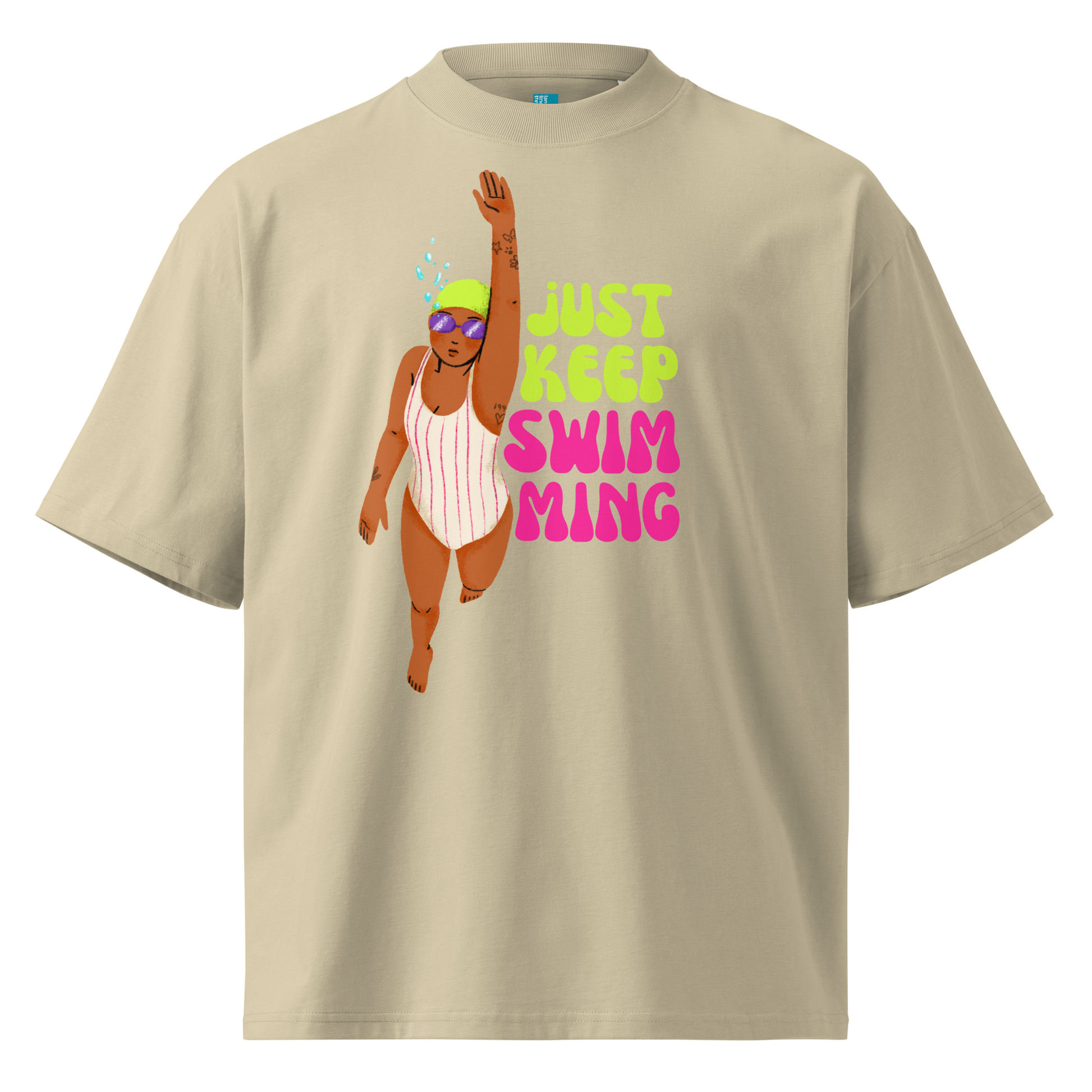 A beige short-sleeve crewneck organic oversized t-shirt featuring a graphic of a woman in a pink and white striped swimsuit with goggles, next to the text 'JUST KEEP SWIM MING' in neon green and pink.