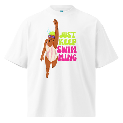 A white short-sleeve crewneck organic oversized t-shirt featuring a colorful graphic of a girl swimmer next to the text 'JUST KEEP SWIM MING' in lime green and pink.
