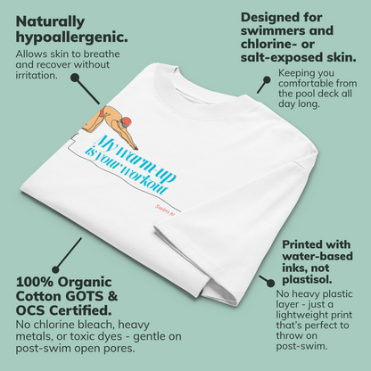 A folded white organic oversized t-shirt with a printed swim-themed graphic and text reading 'My warm-up is your workout' is shown on a pale green background with callout annotations describing product features and benefits.
