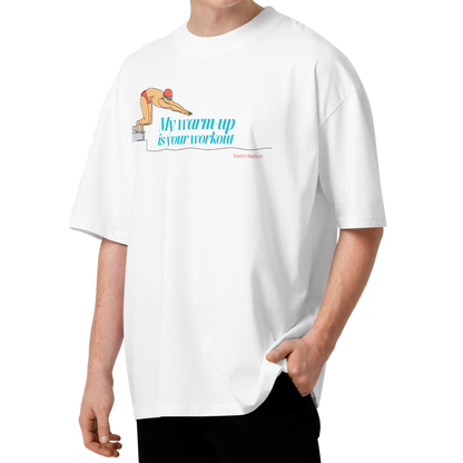 A young man wearing a white short-sleeve crewneck organic oversized t-shirt by Lane Line Threads featuring a graphic of a swimmer on a diving block with the text 'My warm-up is your workout' in blue and 'Swim Nation' in red below, paired with black pants, standing against a solid white background.