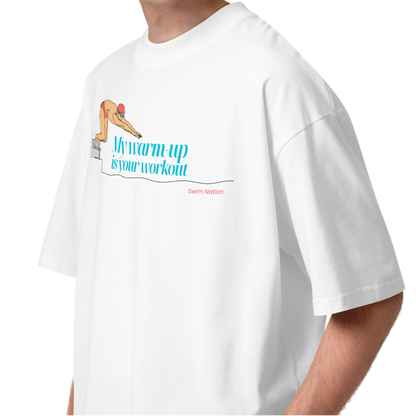 Person wearing a white short-sleeve crewneck organic oversized t-shirt by Lane Line Threads featuring a graphic of a swimmer on a diving block with the text 'My warm-up is your workout' in blue and 'Swim Nation' in red below.