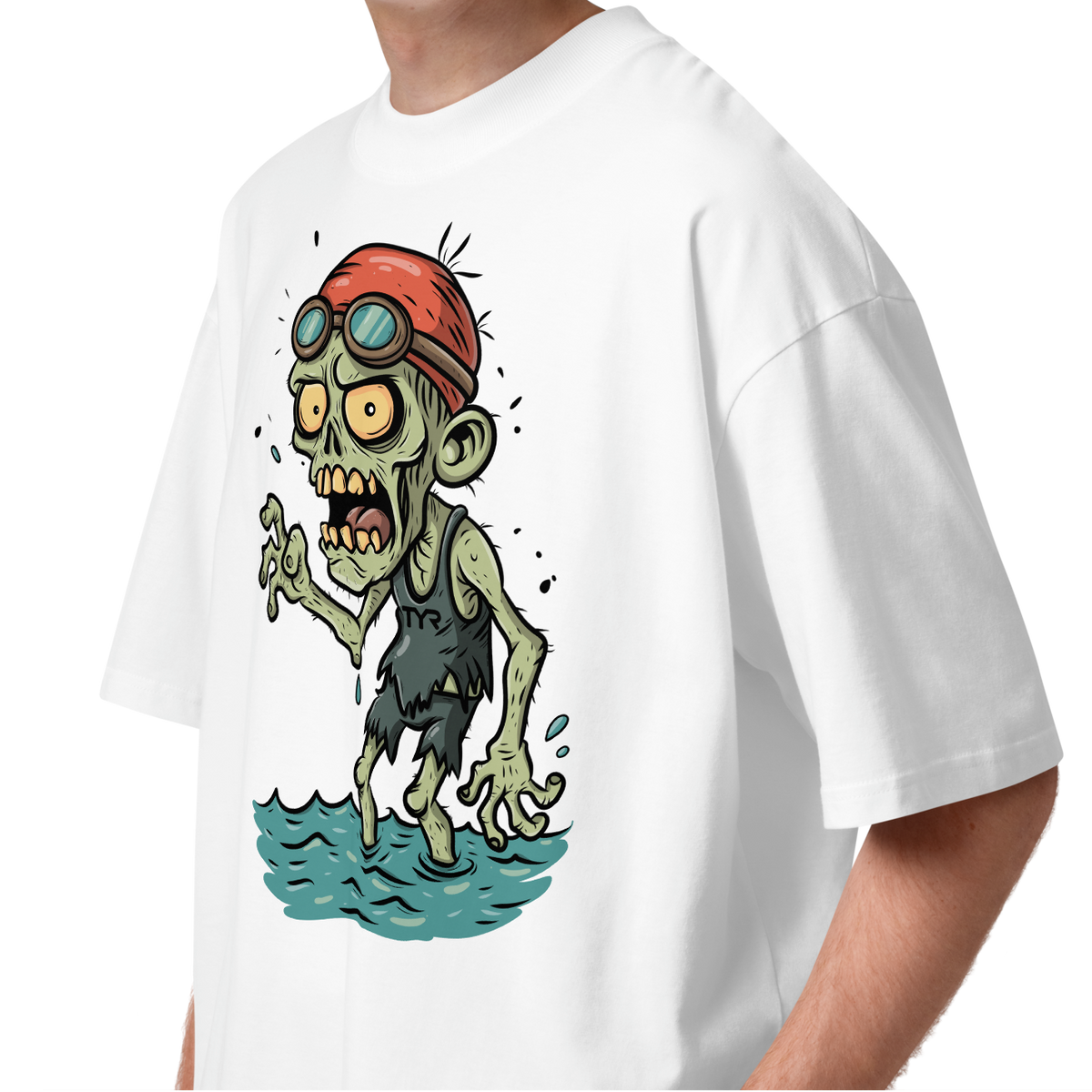 A young man with curly brown hair wearing a white short-sleeve crewneck organic oversized t-shirt by Lane Line Threads, featuring a cartoon graphic of a zombie wearing a red swim cap and goggles, standing in water.