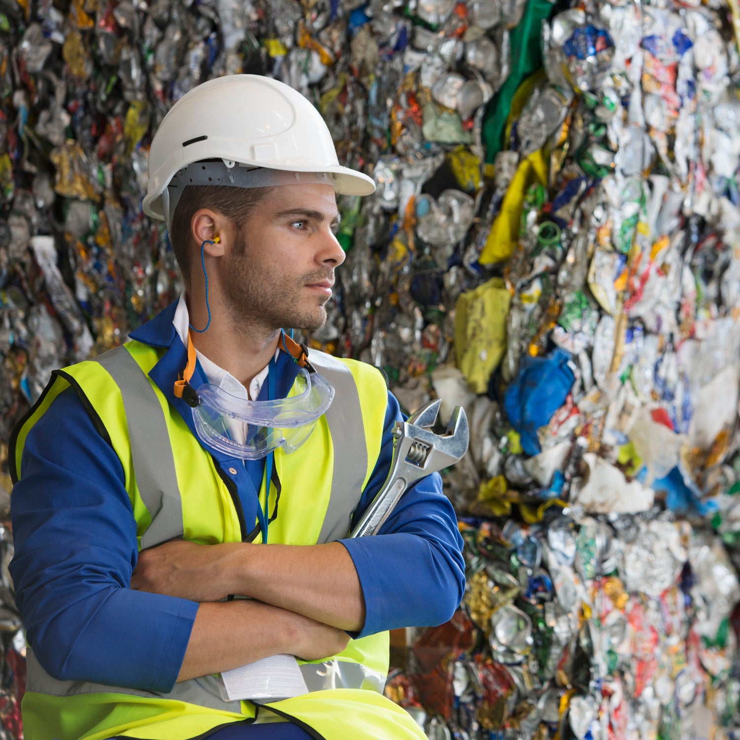 Person in safety gear standing in front of a large pile of recycled materials