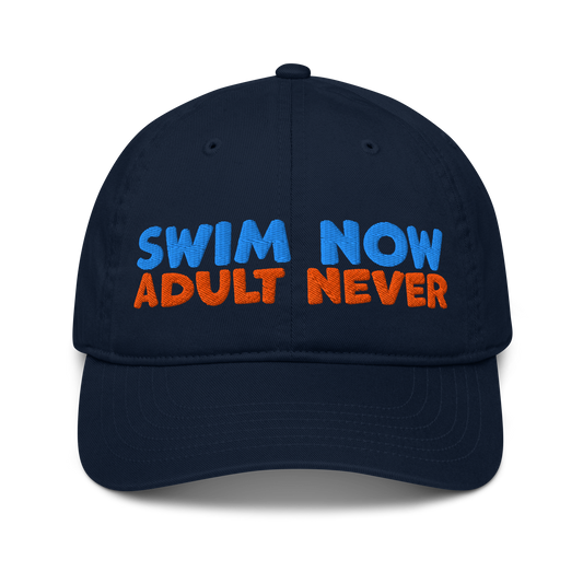Navy blue organic cotton baseball cap with bold blue and orange embroidery reading “Swim Now, Adult Never.” Eco-friendly, vegan, and biodegradable.