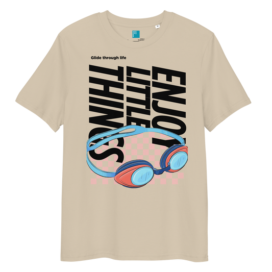 Desert dust eco-friendly t-shirt featuring vibrant blue and red swimming goggles with a checkered background, and bold black text "ENJOY THE LITTLE THINGS" rotated vertically. Above the goggles, "Glide through life" is in smaller text. Made from 100% organic cotton, this breathable and biodegradable shirt is perfect for competitive swimmers who value comfort, performance, and sustainability. Ideal gift for swim meets or lane-protecting athletes with a sense of humor.
