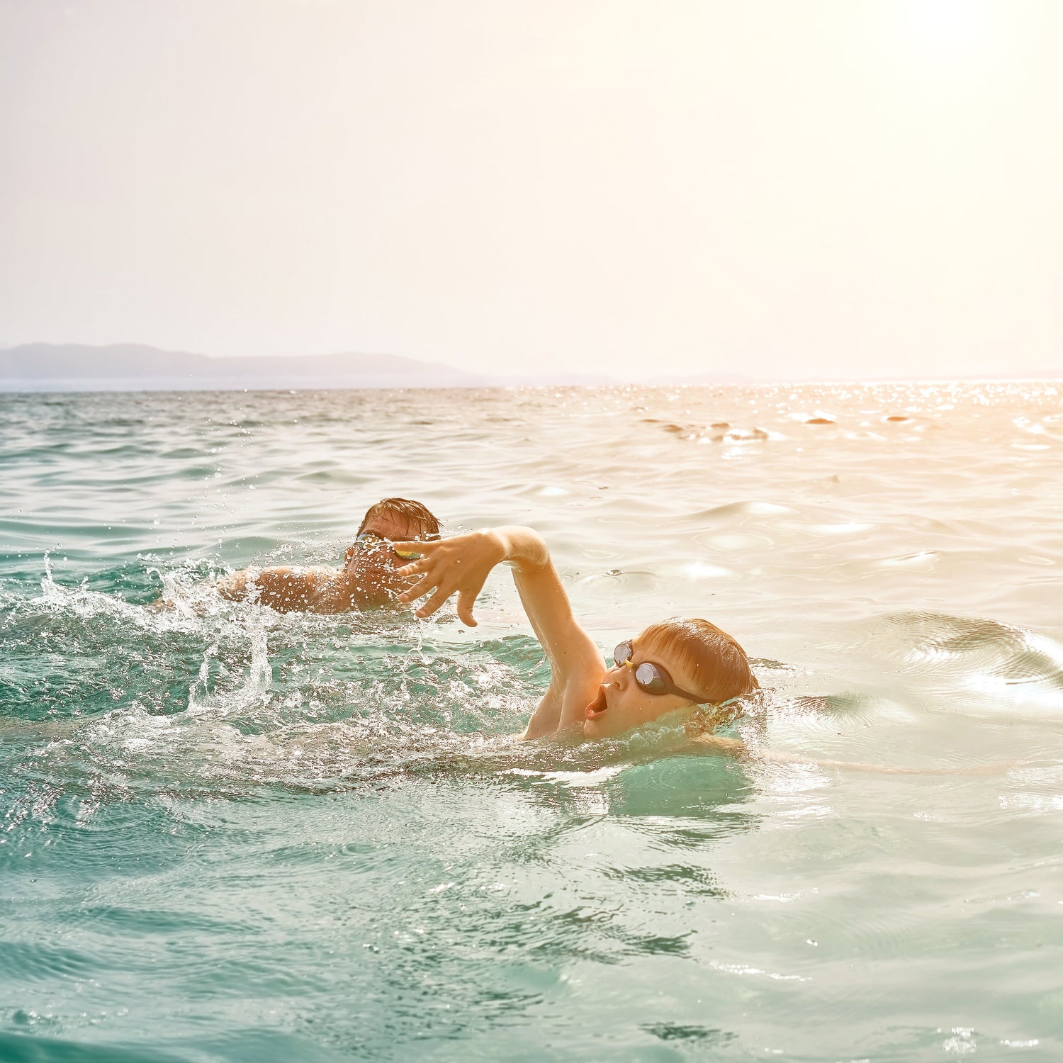 Two people swimming in a body of water with a bright light source in the background